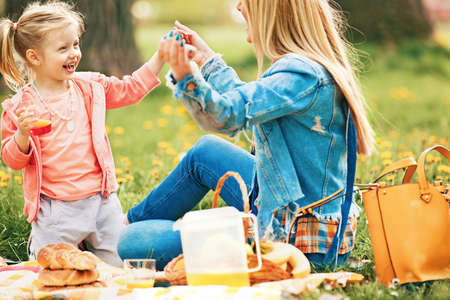 Portrait of happy family of two people. Blonde mum and daughter enjoying picnic in park.の写真素材
