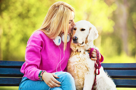Young blonde woman is relaxing in the park with her retriever.の写真素材