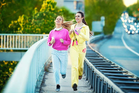 Two attractive and sporty girl friends exercising on the bridge. Living healthy lifestyle.の写真素材