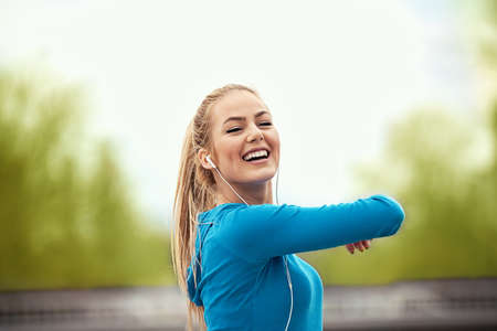 Young blonde woman exercising and listening music on the bridge.の写真素材