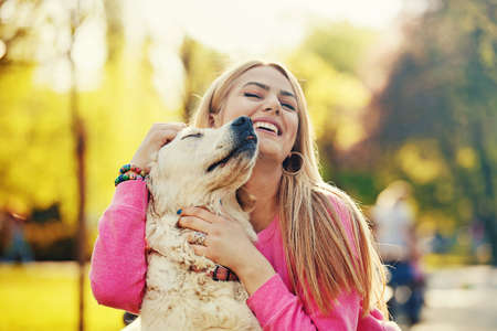 Young blonde woman is relaxing in the park with her retriever.の写真素材