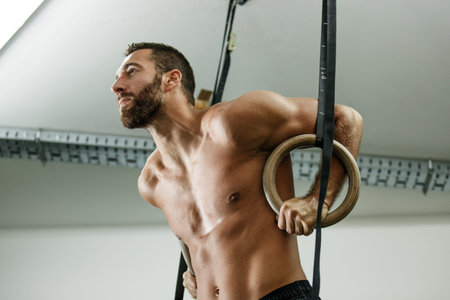 Young fit man is preparing for pulling up on gymnastic rings.