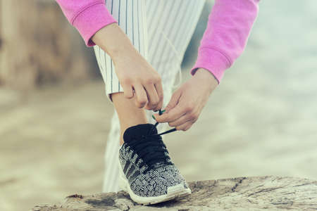 Sportive young woman running on the beach. Taking care about gym shoes. Close up concept.の写真素材