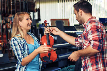 Young woman is buying violin in musical instrument store.の写真素材