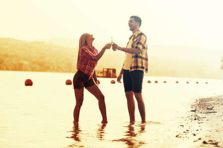 Young couple enjoying free time on the beach and drinking beer.の写真素材