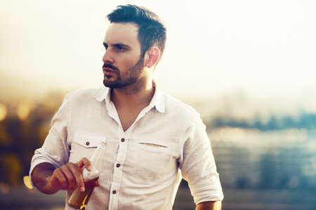 Young handsome man is drinking beer and an enjoying sunset.