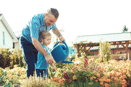 Grandfather is watering flowers with his granddaughter.の写真素材