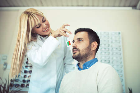 Beautiful blonde ophthalmologist checking eyesight to male patient optics store.の写真素材