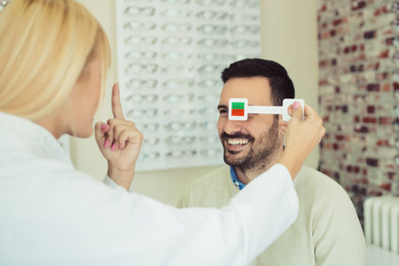 Beautiful blonde ophthalmologist checking eyesight to male patient optics store.