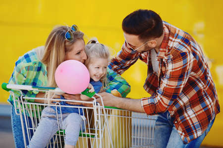 Happy family of three having fun after shopping, in front of supermarket.の写真素材