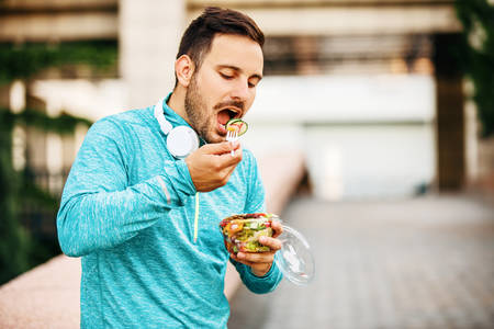 Young handsome man is enjoying vegetable salad after jogging.の写真素材