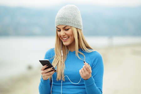 Young blonde woman is relaxing and listening music after training on the beach.の写真素材