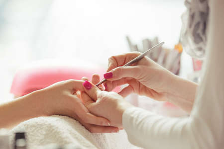 Woman hands receiving manicure and nail care procedure. Close up concept. Manicurist pushing cuticles on female's nails. の写真素材