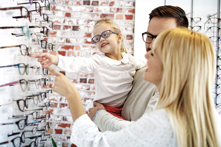 Four year little girl in optics store choosing glasses with her father. Ophtamologist helping. の写真素材