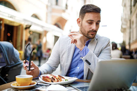 Businessman having breakfast and doing his work in cafe.の写真素材