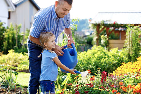 Grandfather is watering flowers with his granddaughter.の写真素材