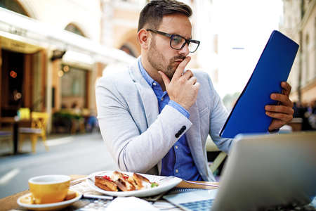 Businessman having breakfast and doing his work in cafe.の写真素材