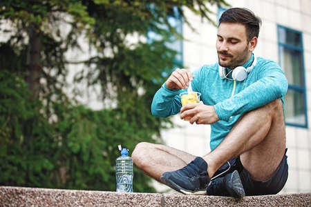 Man is eating fruit salad and relaxing after jogging.の写真素材