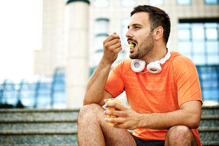 Young handsome man is enjoying fruit salad after jogging.の写真素材