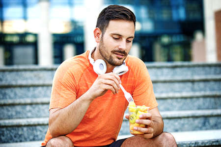 Young handsome man is enjoying fruit salad after jogging.の写真素材