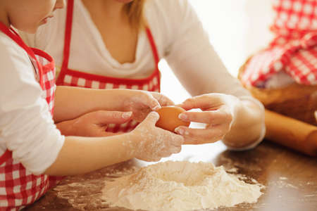 Young mother and her beautiful 4 years old daughter making dough for biscuits. Lifestyle photo. Close up concept.の写真素材