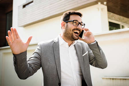 Young smiling businessman is using phone outside.の写真素材
