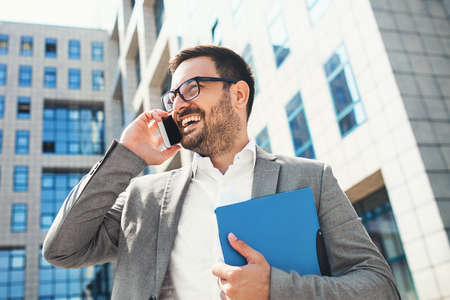 Young businessman using mobile phone in front of company building.の写真素材