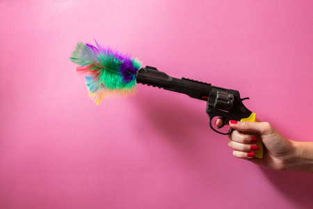Gun, pistol in hand. Colorful feathers come out. Pink background. Cool concept.