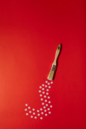 Painting brush leaves a trail of silver shine and white snowflakes on red background. Cool colorful...