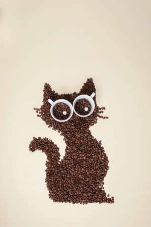 Cool tiny cat made of caffee beans. Light Brown background. Eyes cup of coffee.の写真素材