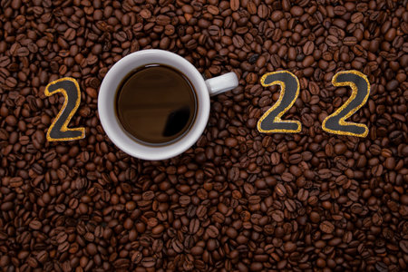 2022. New Year black and gold numbers with coffee mug, cup. With a lots of coffee beans around. Coffee background. Holiday concept.の写真素材