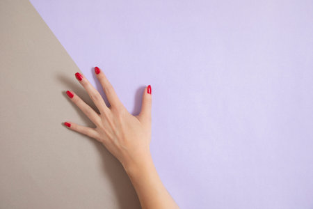 Beautiful female handd with red nail polish, on a purple and gray background