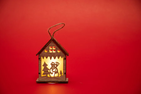 a small wooden house with a snowman and a Christmas tree on a red background. Happy holidays.