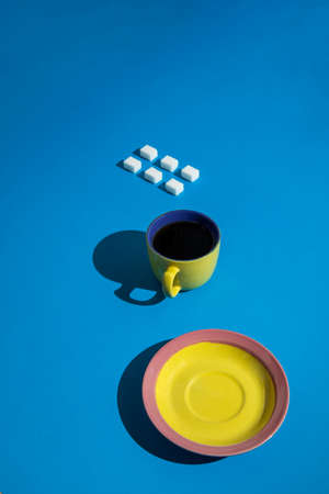 Sugar cubes, yellow a cup of coffee and a yellow-pink tray on a blue background. Great, cool and minimalistic look.の写真素材
