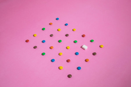 A pattern of sweets, colorful candies and one sugar cube. Pink background.