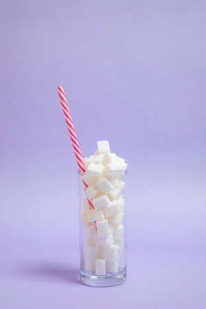 glass full of sugar cubes with a straw inside on a purple background. Cool photo, refreshing joyful idea. Sugar drink.の写真素材