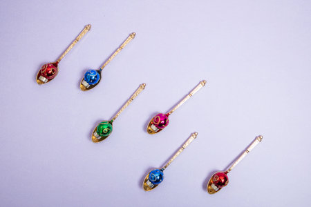 gold spoons with colorful Christmas decorations in them. Purple background