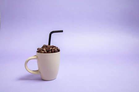 a light brown cup full of coffee beans with a black straw inside. Purple background. good morning with coffee.の写真素材