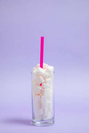 glass full of sugar cubes with a straw inside on a purple background. Cool photo, refreshing joyful idea. Sugar drink.の写真素材
