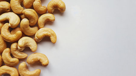 On a white monochrome background, cashew nuts with a characteristic crescent shape and golden hue are located on the left side of the frame, creating the opportunity to add textの素材