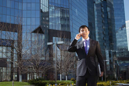 Young businessman standing and talking on mobile phone over business center.の写真素材