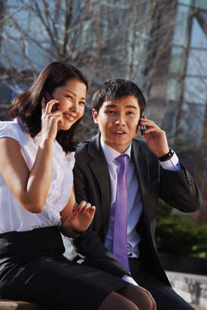 Business couple sitting on the bench chatting with mobile phoneの写真素材