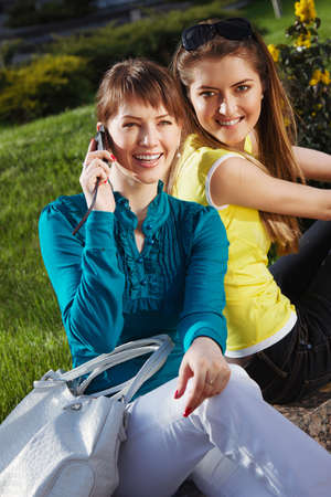 The beautiful girl with girlfriend and talking with cellphoneの写真素材