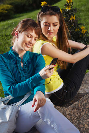 The beautiful girl with girlfriend and talking with cellphoneの写真素材