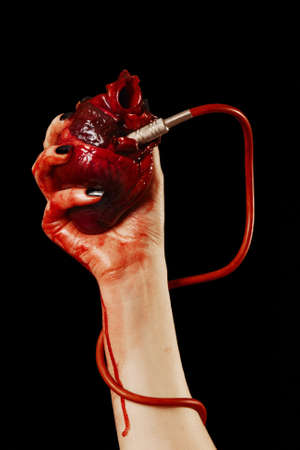 Human heart in hand with pipe, red cable isolated on blackの写真素材