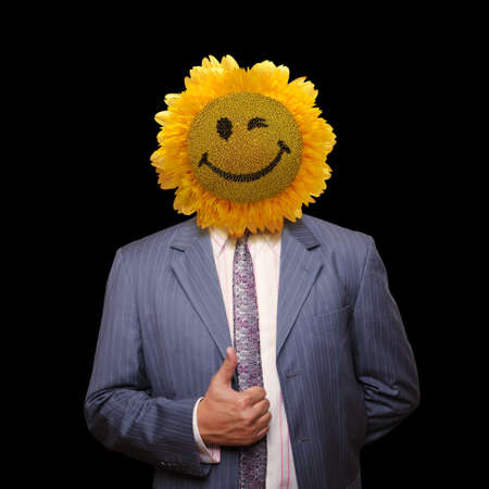 Smiling sunflower head man in suit coat with present thumbs up over blackの写真素材