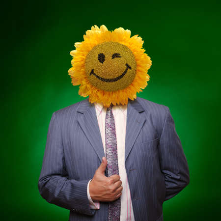 Smiling sunflower head man in suit coat with present thumbs up over greenの写真素材