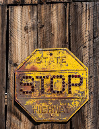 An old, rusty, yellow glass bead stop sign on weathered woodの写真素材