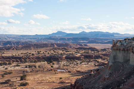 Cliffs give way to a valley floor benath puffy clouds on a blue sky in Utahの写真素材