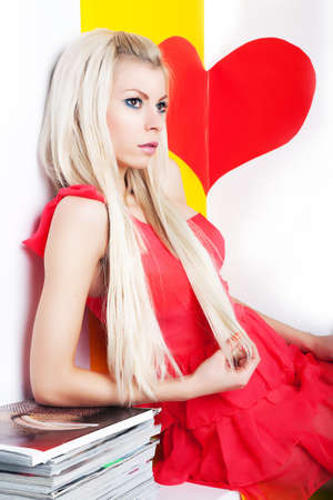 Sexy young woman with beautiful long blond hair, posing in studio in red modern dressの写真素材